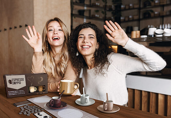 Image of a happy girls friends sitting in cafe talking with each other drinking tea or coffee waving.